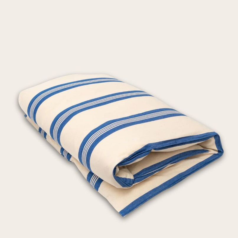 A folded cream-colored cotton mattress topper with blue stripes, shown on a solid light beige background.